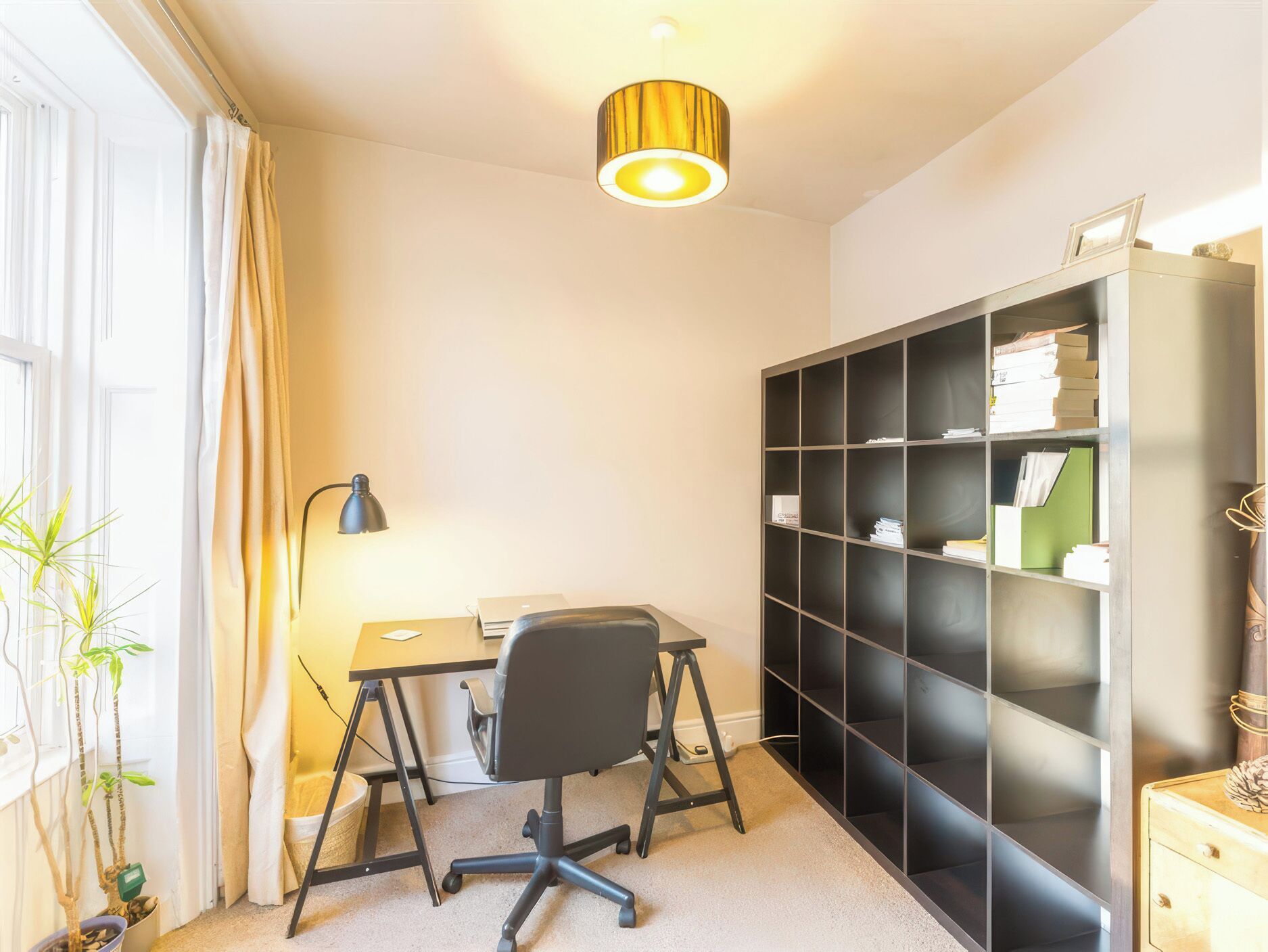 A room with a desk, chair, bookshelf, and a hanging light fixture.