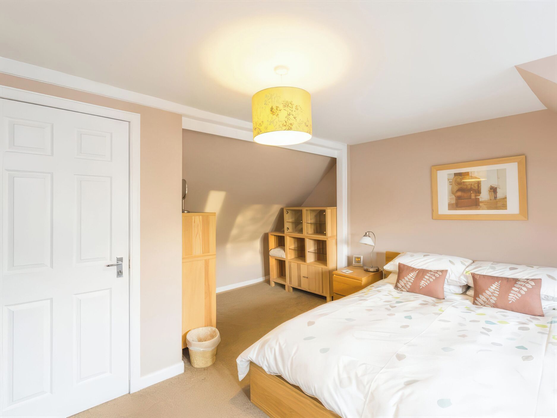 Une chambre à coucher avec un lit, des tables de chevet, une lampe, un tableau au mur et une porte.