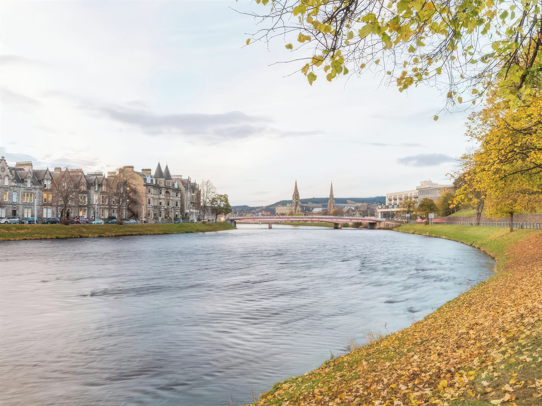 A river with a bridge, historic buildings, and a church spire in the background.
