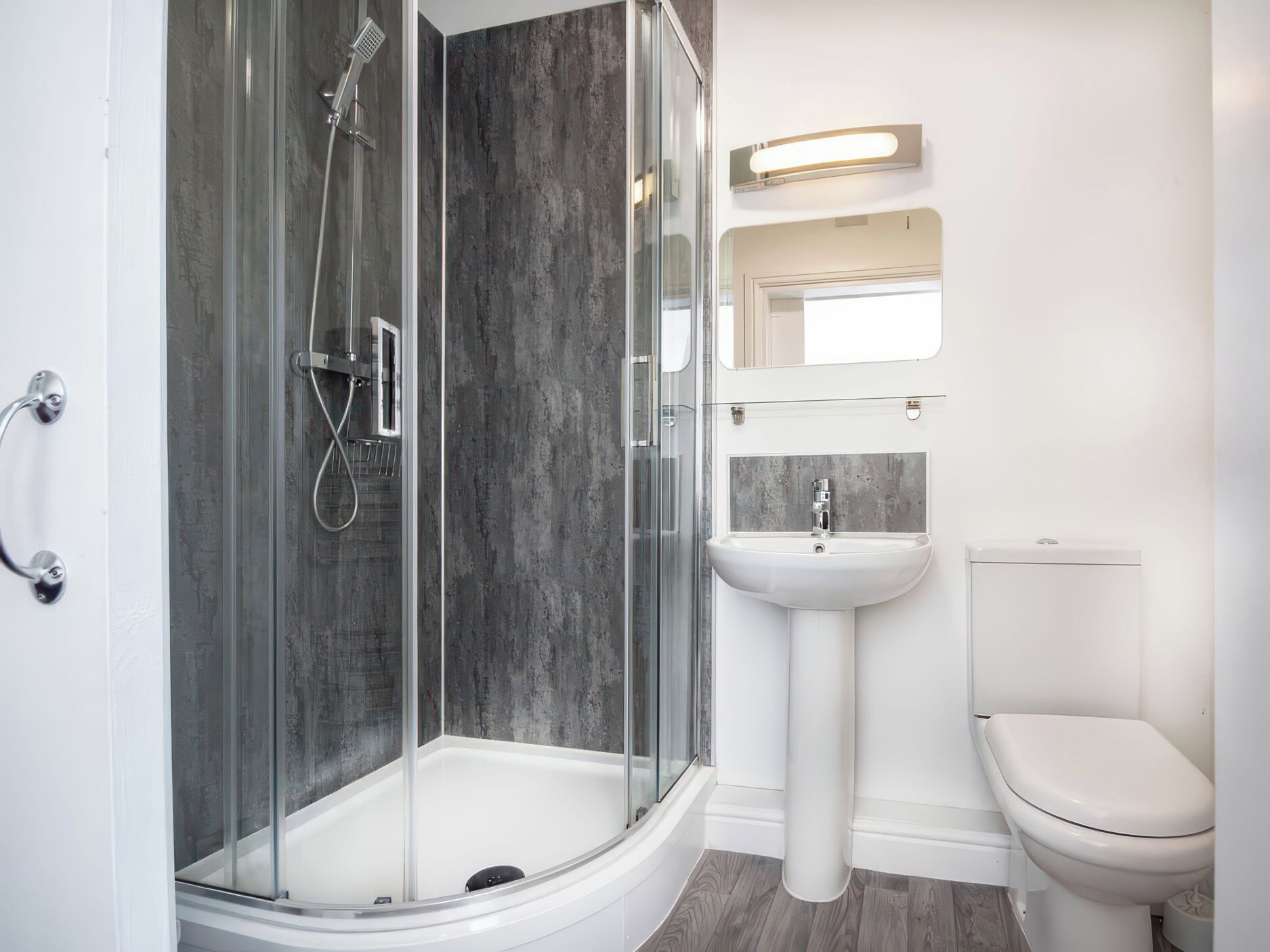 A modern bathroom with a glass-enclosed shower, a pedestal sink, and a toilet.