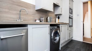 A modern kitchen with a built-in washer and dryer, stainless steel appliances, and light wood cabinetry. - 4 Lower Kessock Street (Inverness)