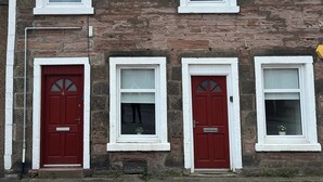 A row of three-story stone buildings with red doors and white-framed windows. - 4 Lower Kessock Street (Inverness)