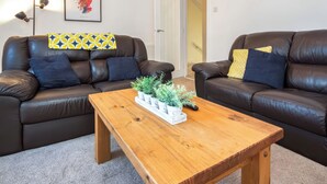 A living room with two brown leather sofas, a wooden coffee table, and a framed cityscape picture on the wall. - 4 Lower Kessock Street (Inverness)