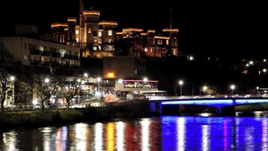 A nighttime view of a castle-like building with a bridge over a reflective water body. - 4 Lower Kessock Street (Inverness)