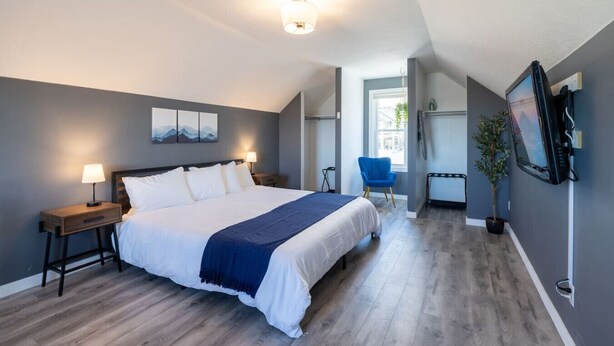 A modern bedroom with a large bed, bedside tables, a desk, a chair, and a TV. - Lone Peak View | Pickleball + Putting Green (Draper)