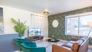 A modern living room with a sofa, teal chairs, a TV, and a large window. - Lone Peak View | Pickleball + Putting Green (Draper)