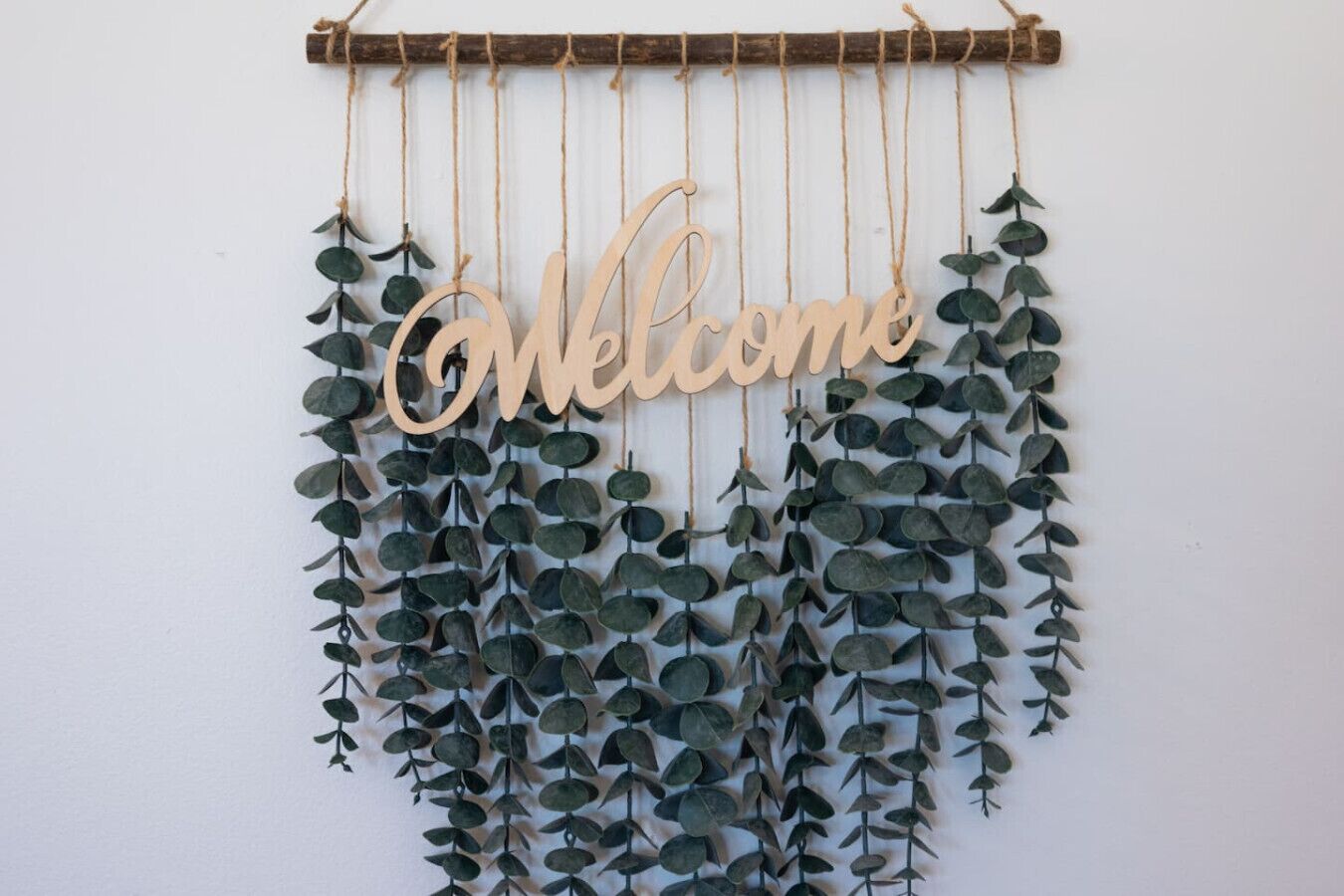 Decoración de pared con un cartel de 'Welcome' y hojas de eucalipto colgantes.