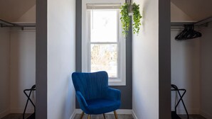 A room with a blue armchair, a window with a view, and a hanging plant. - Lone Peak View | Pickleball + Putting Green (Draper)