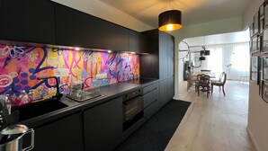 A modern kitchen with a colorful backsplash, black cabinets, and a dining area with a chandelier.