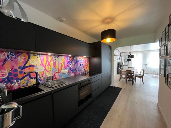 A modern kitchen with a colorful backsplash, black cabinets, and a dining area with a chandelier.