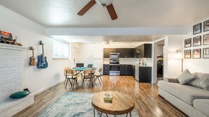 A modern living room with a fireplace, a dining area, a kitchen, and a ceiling fan.