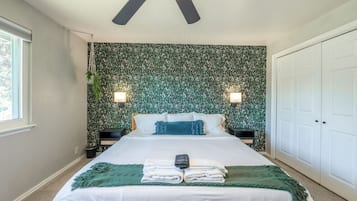 A bedroom with a bed, bedside lamps, a ceiling fan, a green wall, and a white door.
