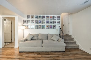 A living room with a sofa, framed pictures on the wall, and a staircase. - Hot Tub & Pickleball | Packed with Entertainment | Near BYU (Orem)