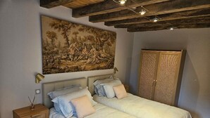A bedroom with two beds, a large painting above the beds, a nightstand with a lamp, and a woven basket. - Authentic cottage in Auvergne, 8 pers, pets allowed (Autry-Issards)