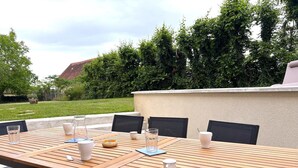 An outdoor dining area with a wooden table and black chairs, surrounded by greenery and a stone wall. - Authentic cottage in Auvergne, 8 pers, pets allowed (Autry-Issards)