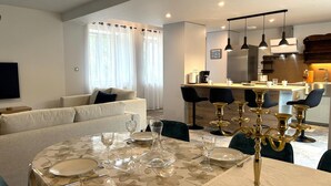 A modern living room with a sofa, a dining table set for four, and a kitchen area in the background. - Authentic cottage in Auvergne, 8 pers, pets allowed (Autry-Issards)