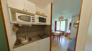 Cocina compacta con microondas, pileta y estufa. Se ve un comedor con mesa y sillas a través de un umbral abierto.