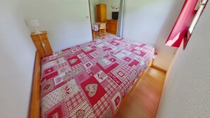 Un dormitorio con cama, mesita de noche de madera, espejo y ventana con cortinas.