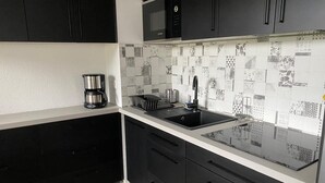 A modern kitchen with black cabinets, a black countertop, and a patterned backsplash.