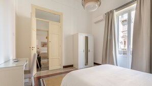 A hotel room with a bed, a desk, a wardrobe, and a door leading to another room. - Casa Markea by Wonderful Italy (Palermo)