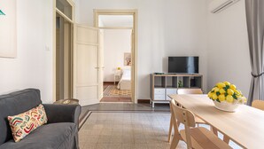 A modern living room with a grey sofa, a dining table with chairs, a TV, and a basket of lemons. - Casa Markea by Wonderful Italy (Palermo)