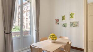 A dining area with a table, chairs, and a vase of yellow flowers. There are curtains on the window, and artwork on the wall. - Casa Markea by Wonderful Italy (Palermo)