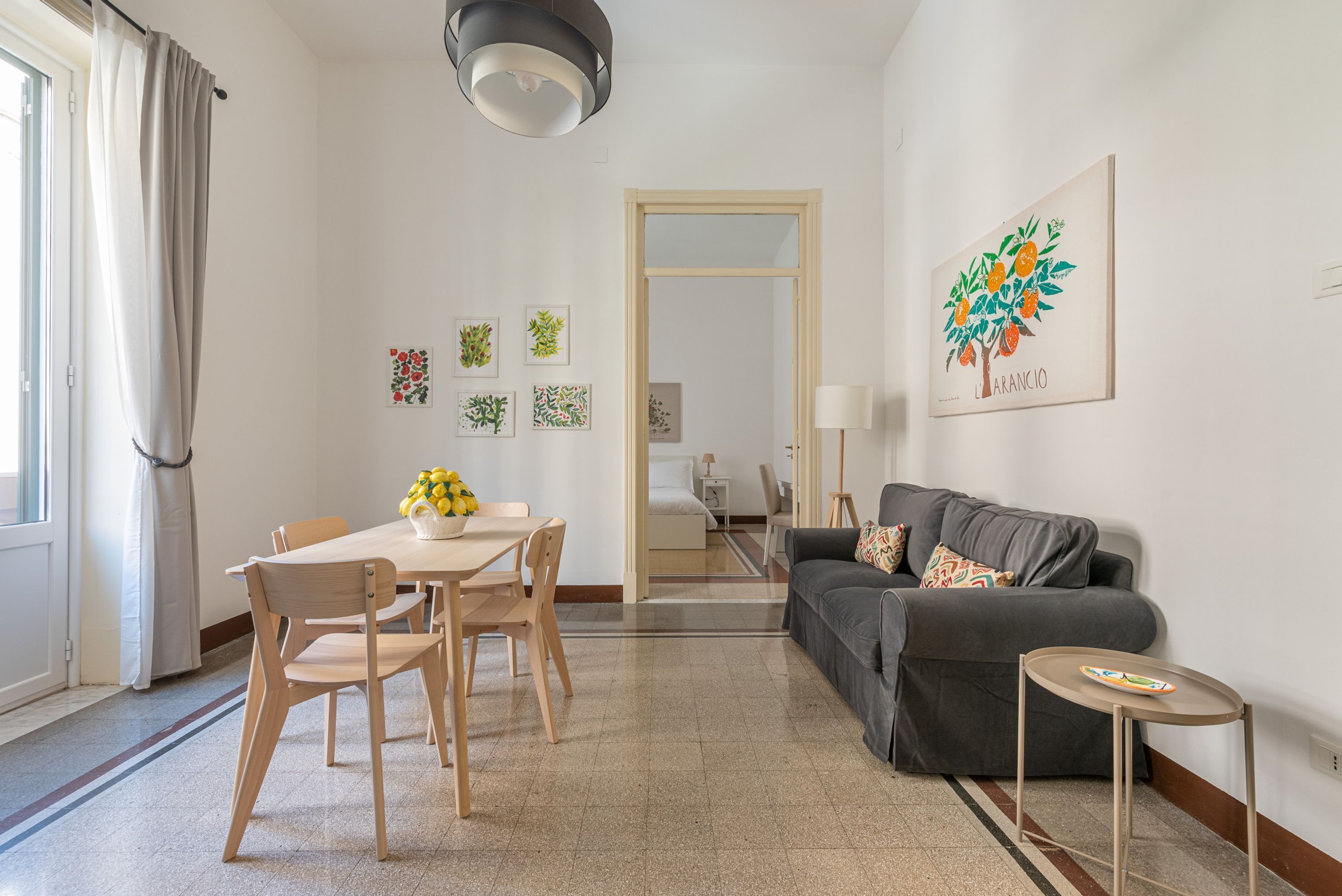 Uma sala de estar moderna com área de jantar, um sofá cinza e uma mesinha com abajur.