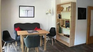 A modern living room with a wooden dining table, two black chairs, a black sofa, and a bookshelf. - Apartments "Laber" for 2 persons, with kitchen (Oberammergau)