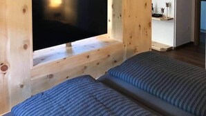A room with a wooden wall-mounted TV, two beds with striped bedding, and a white shelf with decorative items.