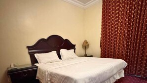 Ein ordentlich bezogenes Bett mit weißen Leinen in einem Hotelzimmer mit rotem Teppich und einem dunklen Holz-Kopfteil.