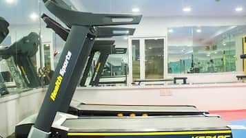 Una cinta de correr con pantalla digital y panel de control, ubicada en un gimnasio con paredes de espejo y equipamiento de ejercicio.