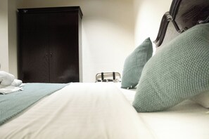 Una cama con ropa blanca, un armario de madera oscura y una mesita de noche con lámpara.