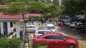 A parking area with several cars and motorcycles, surrounded by buildings with red-tiled roofs and greenery. - Desa Retreat Kuala Kangsar (Kuala Kangsar)