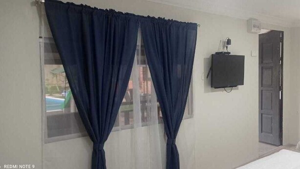 A room with a bed, a TV mounted on the wall, and a window with curtains. - Desa Retreat Kuala Kangsar (Kuala Kangsar)