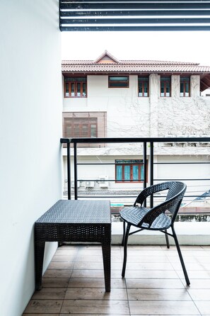 Un balcón con una mesa y silla de metal negro, suelo de baldosas y vistas a un edificio con techo y ventanas a juego.