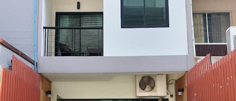 A modern two-story building with a balcony, a small outdoor seating area, and a gated entrance.
