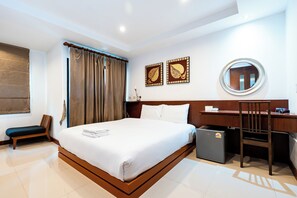 Habitación de hotel con cama, escritorio, silla, refrigerador pequeño y ventana con cortinas.