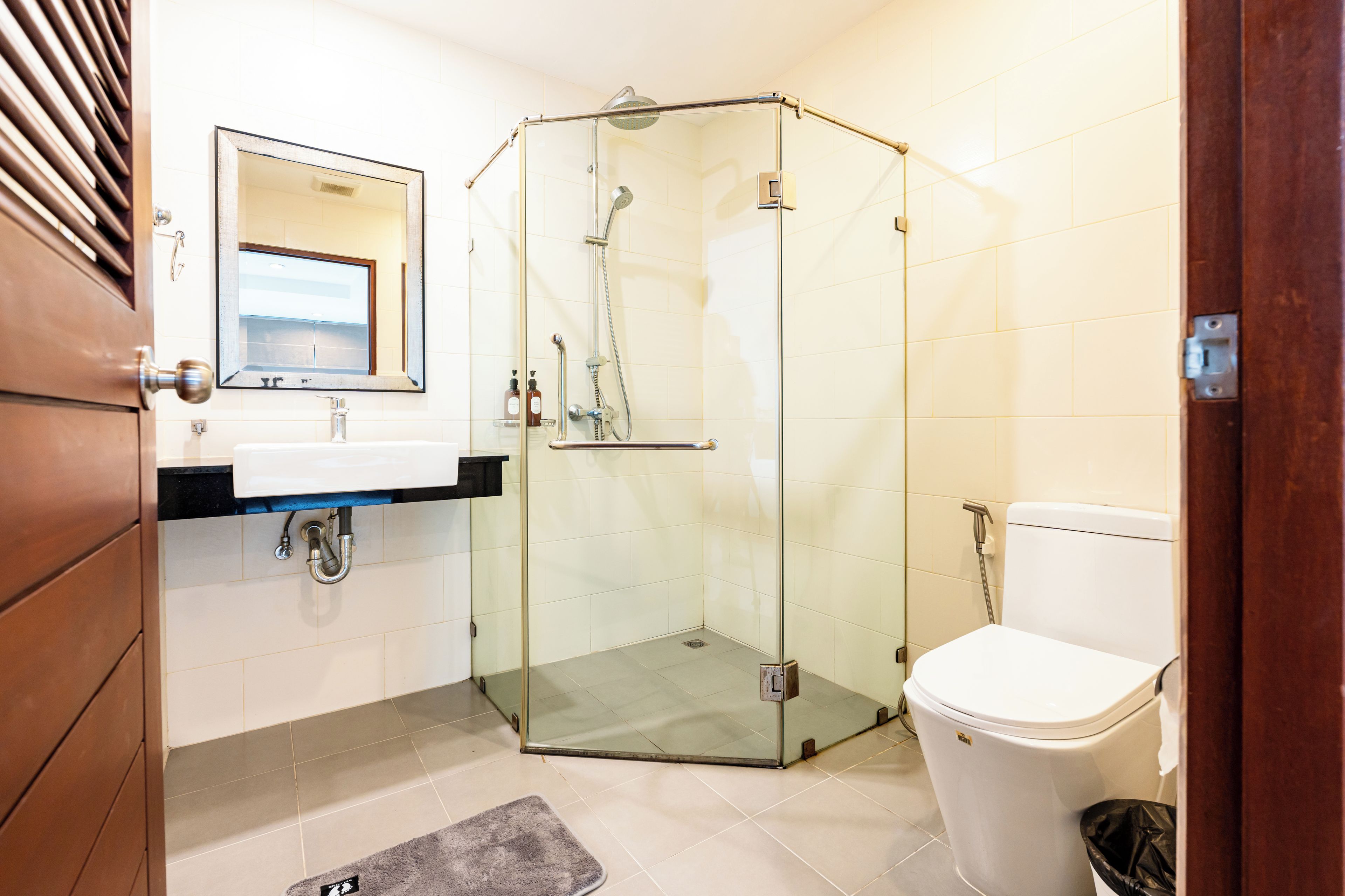 Un baño moderno con ducha envuelta en vidrio, inodoro blanco y lavamanos con espejo superior.