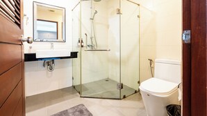 Un baño moderno con ducha envuelta en vidrio, inodoro blanco y lavamanos con espejo superior.