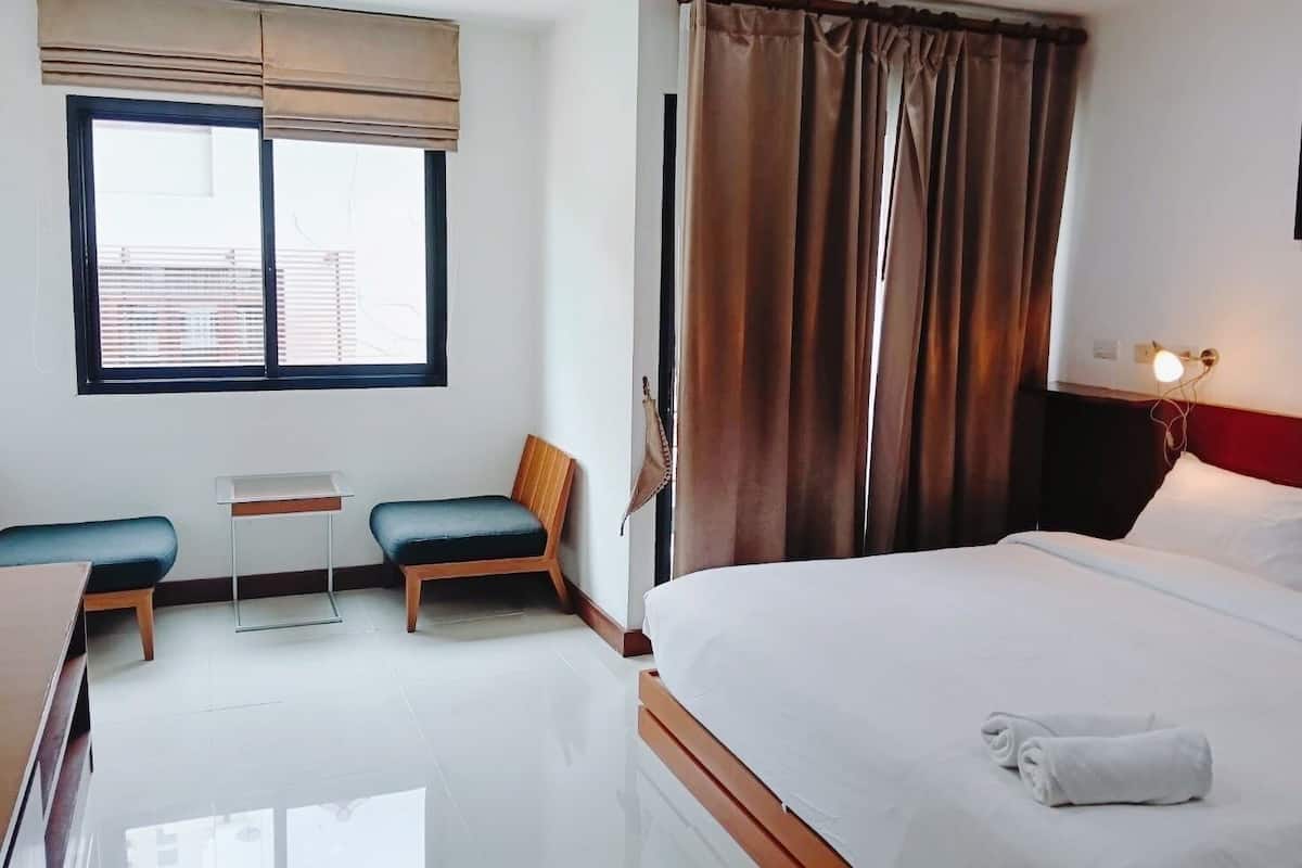 Une chambre d’hôtel comprenant un lit, un bureau avec une chaise, une petite table et une fenêtre avec des stores.