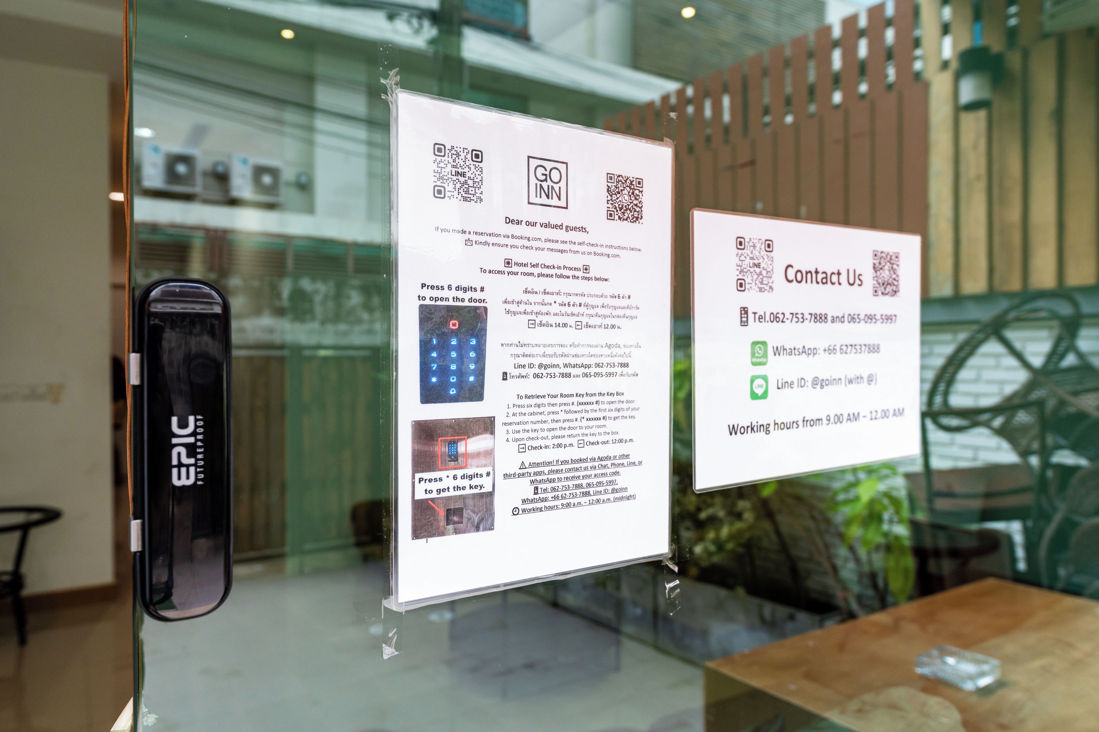 A glass door with informational signs about hotel self-check-in procedures and contact details.