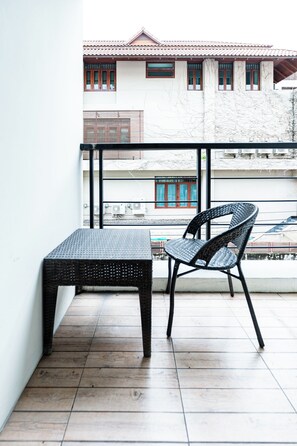 A balcony with a black wicker chair and a matching table, a tiled floor, and a view of a building with a tiled roof and windows. - Yon INN Sukhumvit 4 - BTS Nana (Bangkok)