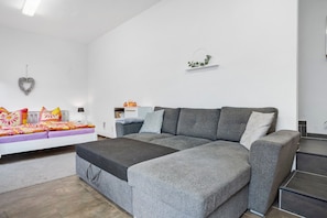 A modern living room with a grey sectional sofa, a white sofa with colorful cushions, a small table, and a heart-shaped decoration on the wall. - Holiday Apartment 'For 2 - 4 People' with Shared Terrace and Wi-Fi (Neukalen)
