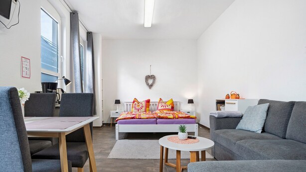 Un salon moderne avec un canapé, une table à manger et un lit agrémenté d’une literie aux couleurs vives.