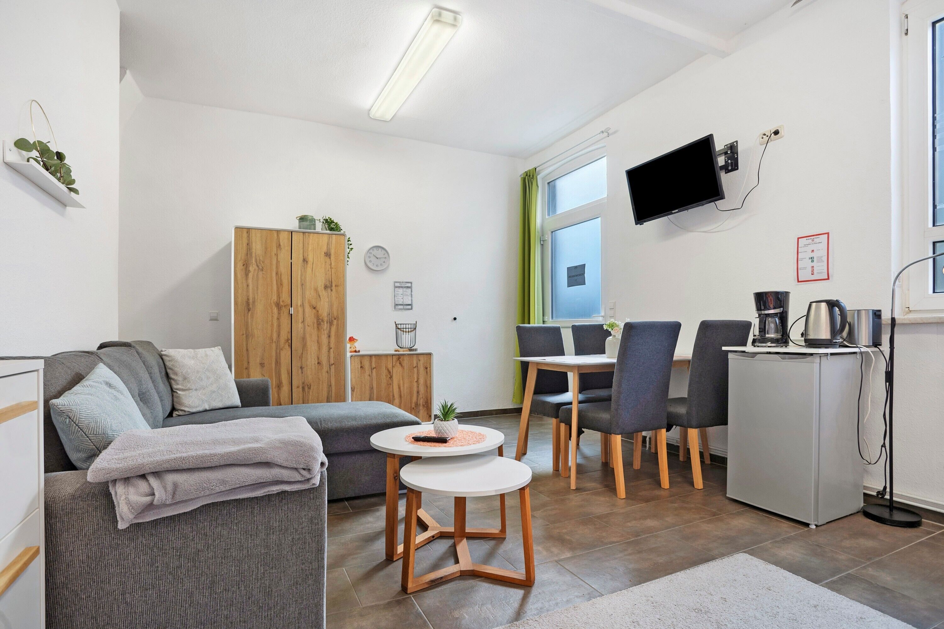Ein modernes Wohnzimmer mit einer Couch, einem kleinen runden Tisch, einem Schrank und einem an der Wand befestigten Fernseher.
