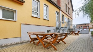 Un bâtiment jaune à la façade en briques, doté de bancs en bois à l’extérieur et d’un chemin piétonnier dallé.