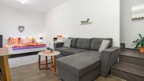 Un salon moderne avec un canapé d’angle, une petite table ronde et un élément décoratif en forme de cœur accroché au mur.