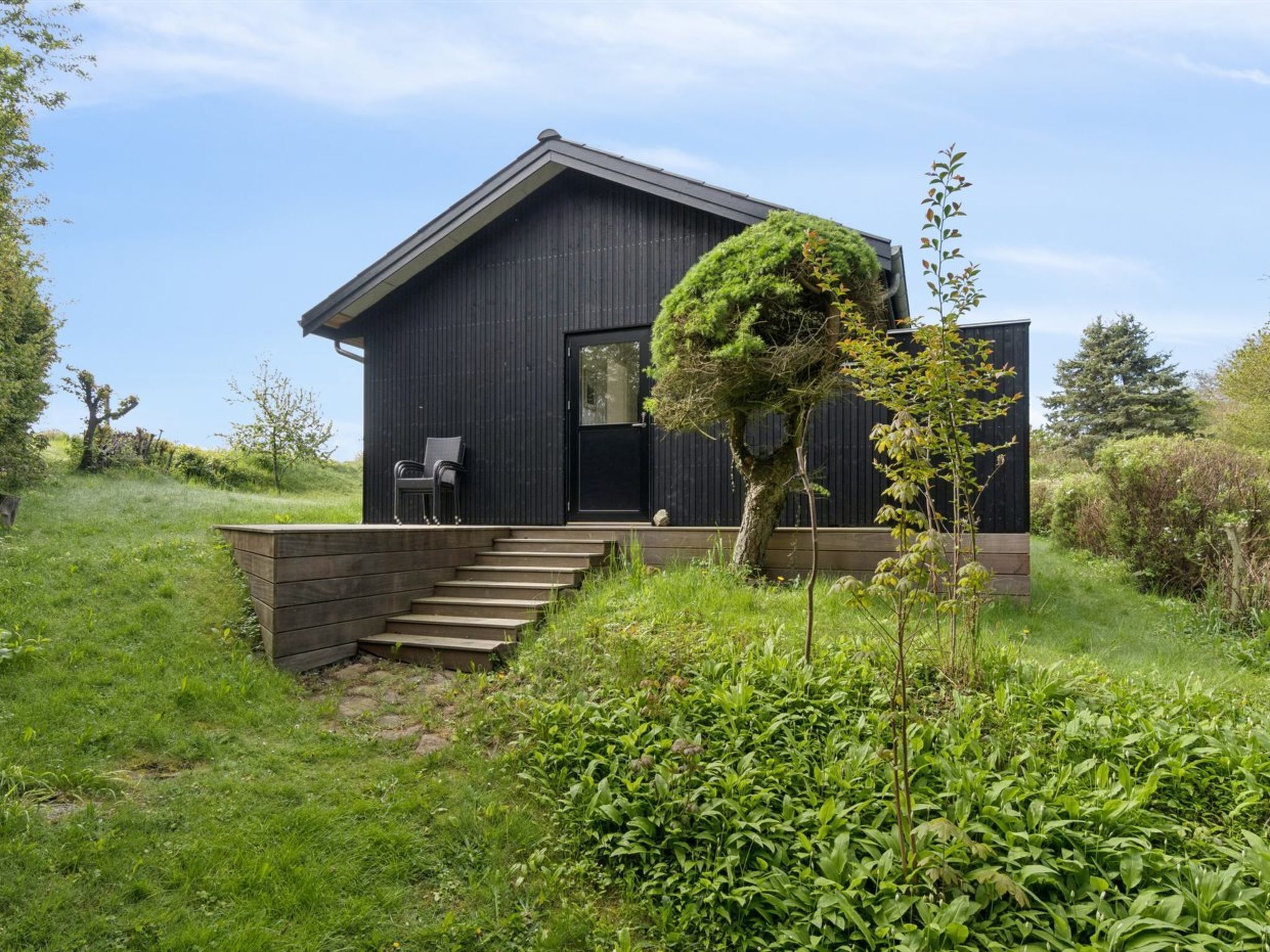 Een modern huis met een donkere gevel, een klein portaaltje met treden en een boom ervoor.