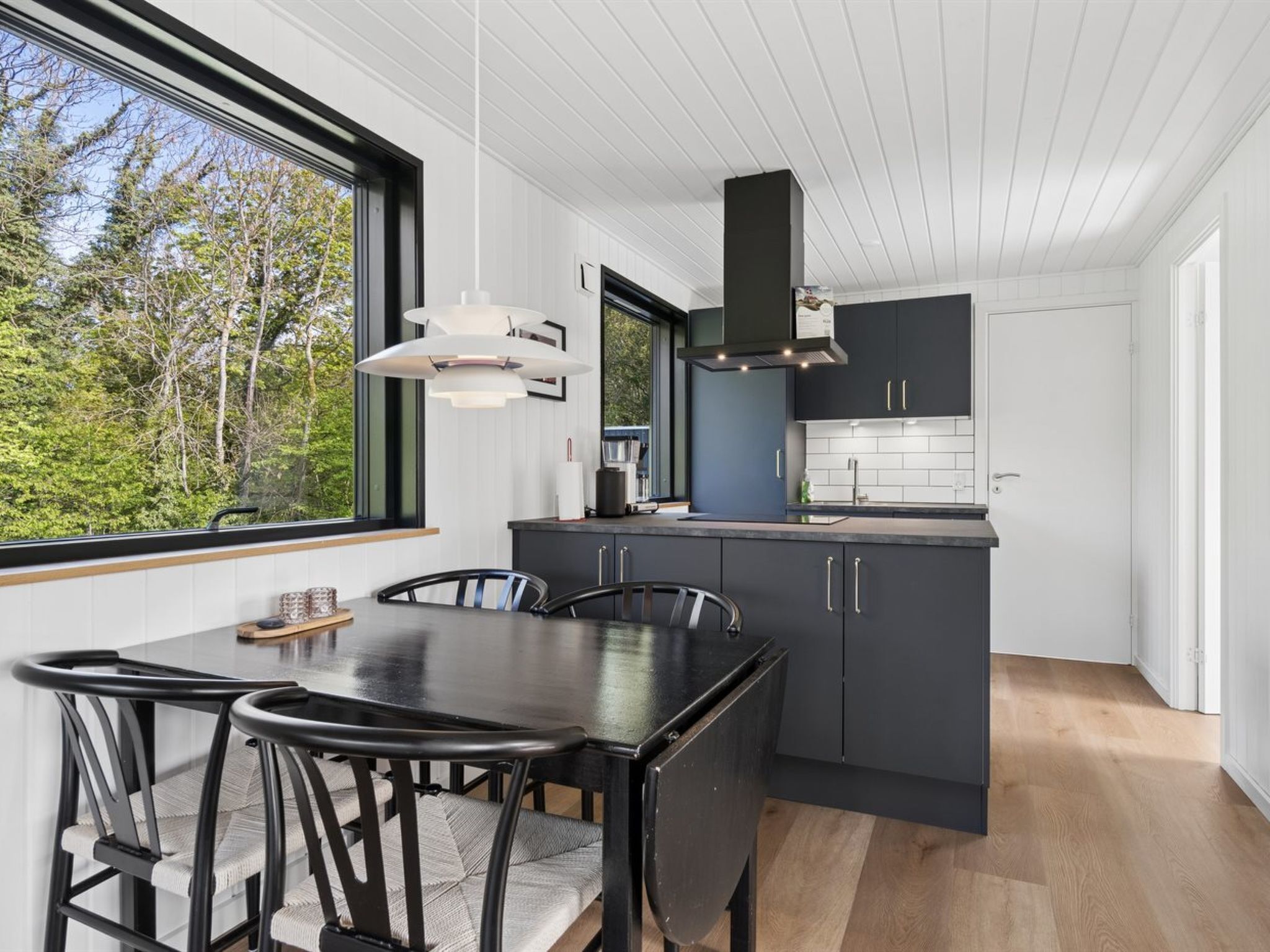 A modern kitchen with dark cabinetry, a large window, and a dining area with a table and chairs.