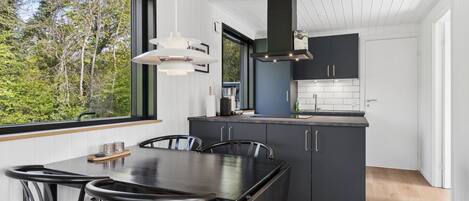 A modern kitchen with dark cabinetry, a large window, and a dining area with a table and chairs.